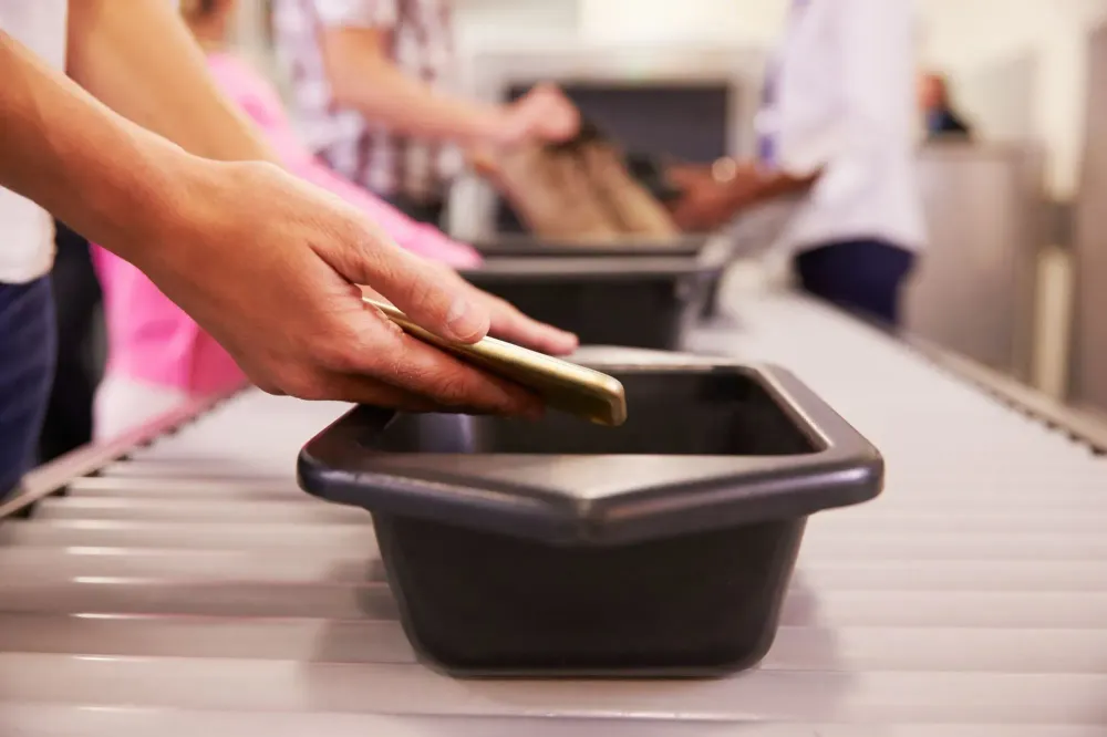 Close up of person's hands putting phone in airport security line bin
